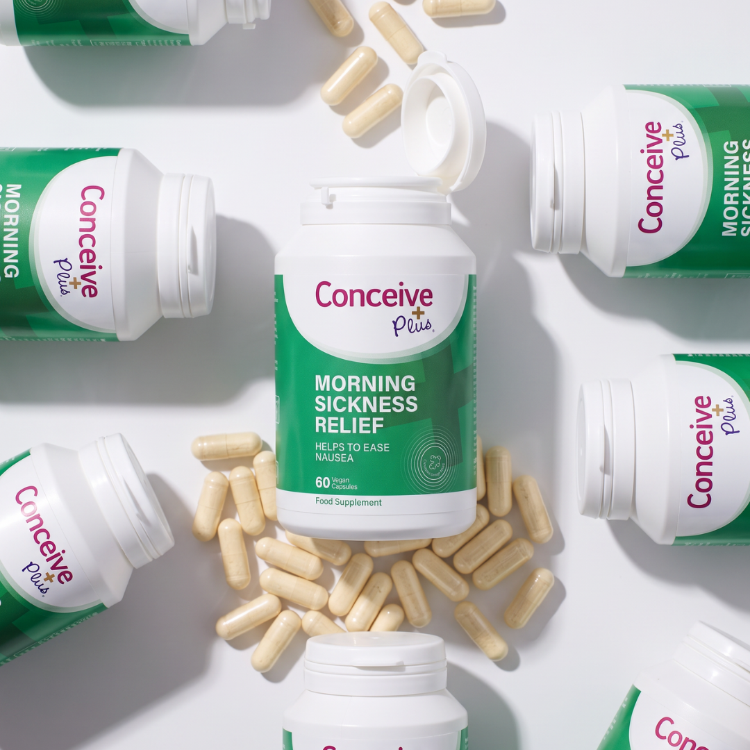 Conceive Plus Morning Sickness Relief dietary supplement bottles and loose beige capsules arranged in a flat-lay composition on a white background.
