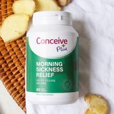 A bottle of Conceive Plus Morning Sickness Relief dietary supplement placed on a white fabric surface next to sliced ginger and a woven basket.