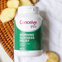 A bottle of Conceive Plus Morning Sickness Relief dietary supplement placed on a white fabric surface next to sliced ginger and a woven basket.