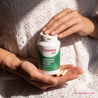 Person holding a bottle of Conceive Plus morning sickness relief supplement with pills in their hand.