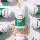 Conceive Plus Morning Sickness Relief dietary supplement bottles and loose beige capsules arranged in a flat-lay composition on a white background.
