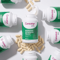 Conceive Plus Morning Sickness Relief dietary supplement bottles and loose beige capsules arranged in a flat-lay composition on a white background.