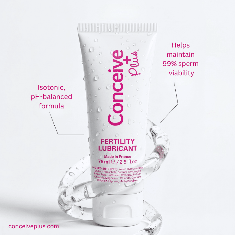 A white tube of Conceive Plus Fertility Lubricant with pink text, shown on a light gray background with decorative clear glass rings. Pink callout text highlights product features.